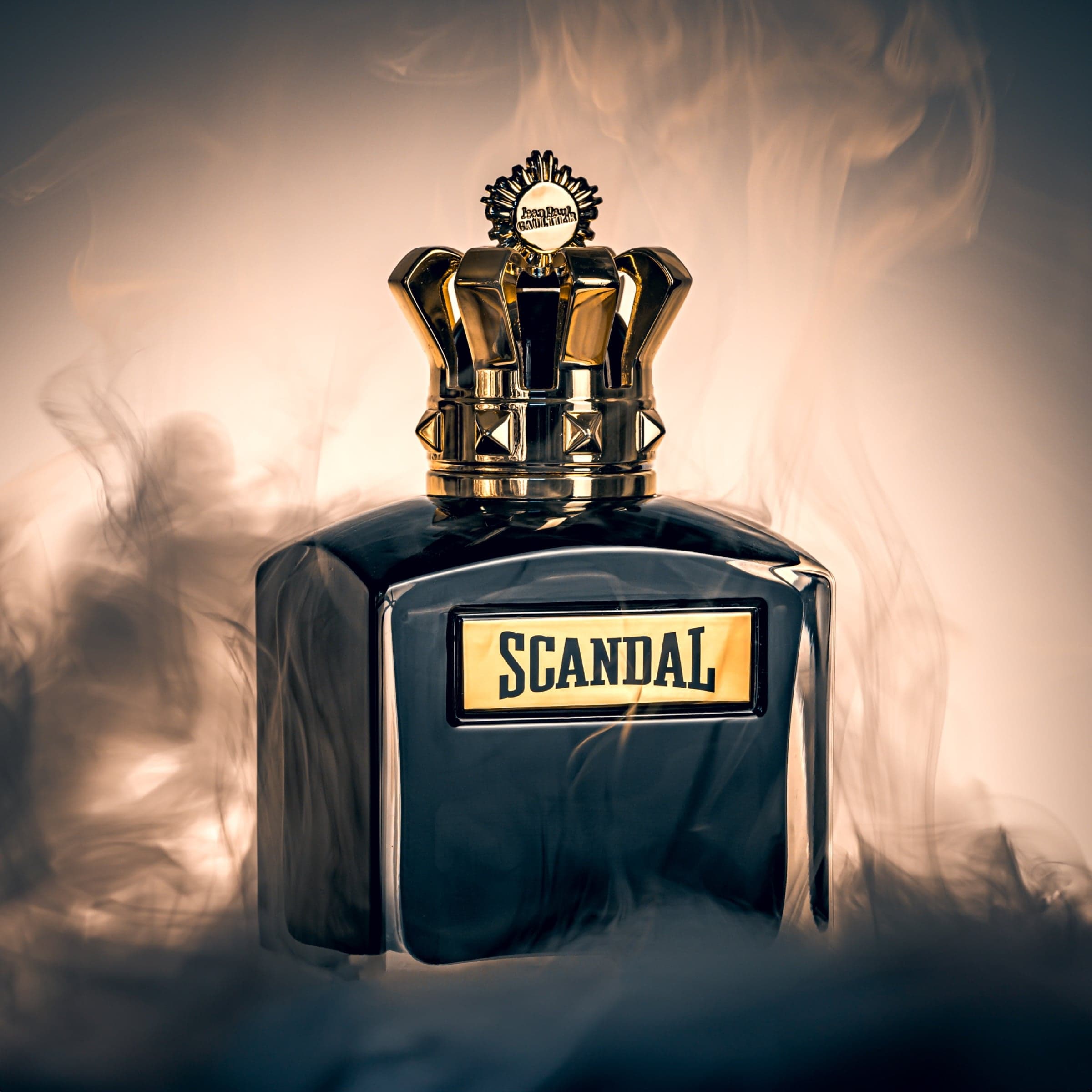 Jean Paul Gaultier Scandal parfumflacon met gouden kroonkop, gefotografeerd in wervelende rookslierten tegen warme achtergrondverlichting