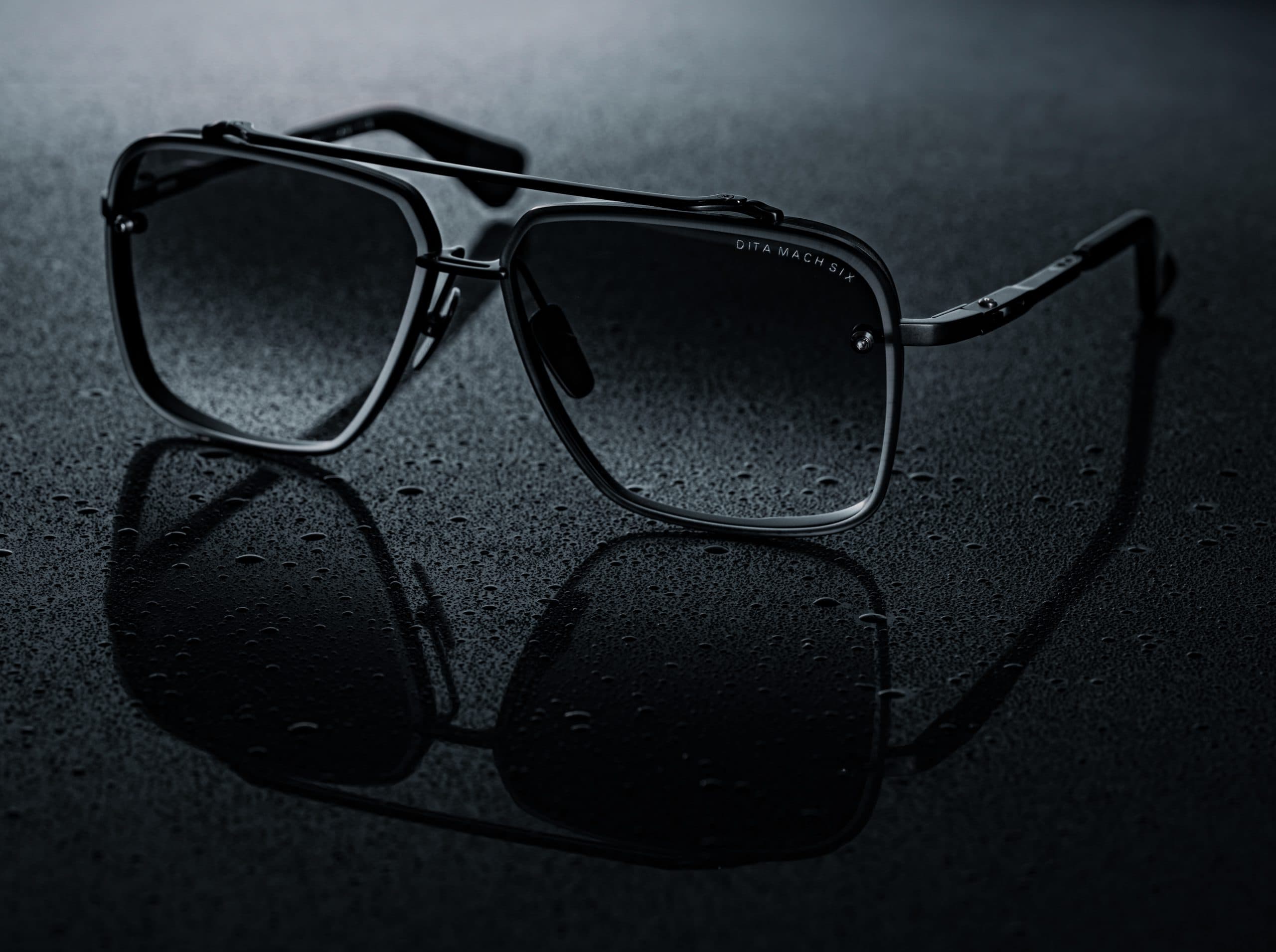 Zwarte Dita Mach-Six zonnebril op een natte donkere ondergrond met waterdruppels, gespiegeld onder studiolicht